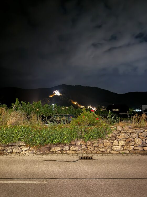 Steinmauer an der Straße bei Nacht, dahinter die angestrahlte Ruine Dürnstein