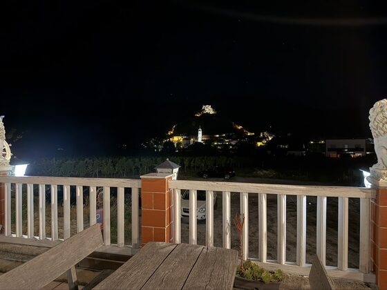 Terrasse bei Nacht mit Holztisch, weißem Geländer und zwei beleuchteten Löwenfiguren, dahinter der Weingarten und das beleuchtete Dürnstein